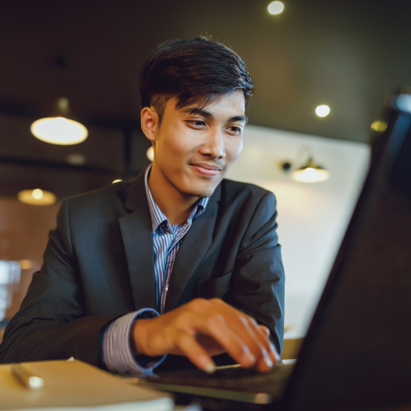 A person in a suit typing on a laptop, engaged in Docusign, with a modern café background.