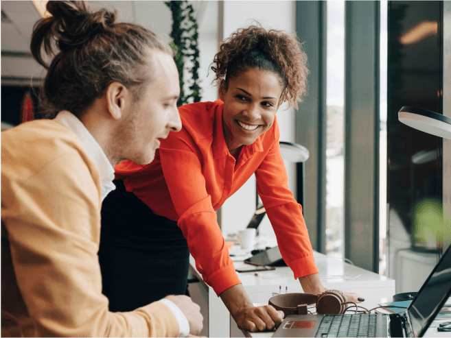 Two professionals collaborate at a desk, discussing Docusign on a laptop, with a modern office backdrop.