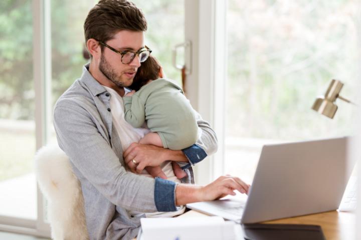 Un hombre lleva su bebe mientras mira su computadora sobre tema de seguridad bancaria