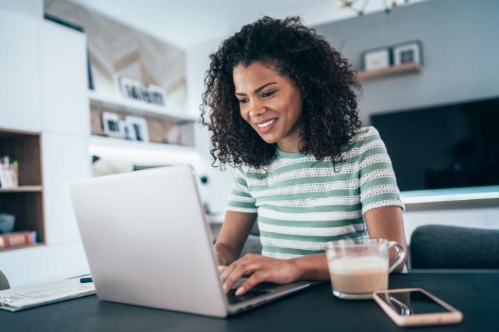 Mulher trabalhando no computador e ao lado xícara de café com leite