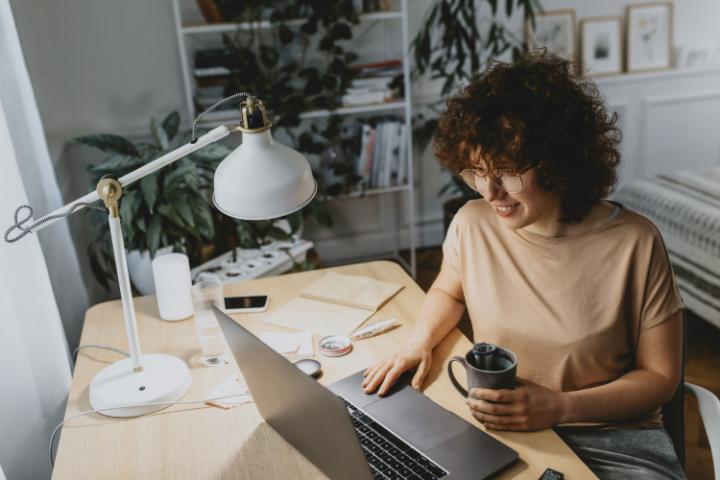 Una mujer toma su té mientras trabaja en su computadora 