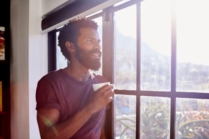 Un hombre toma café al lado de una ventana en un día soleado 