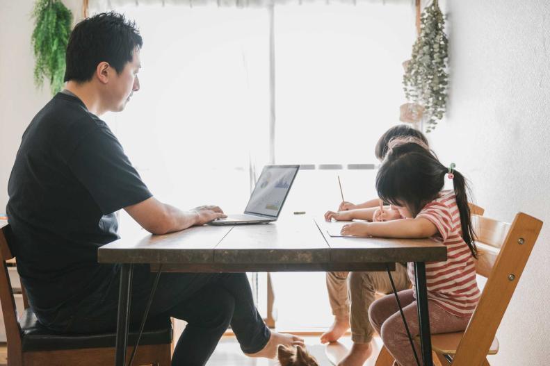 Un padre trabaja desde casa en su computadora mientras sus hijas diseñan