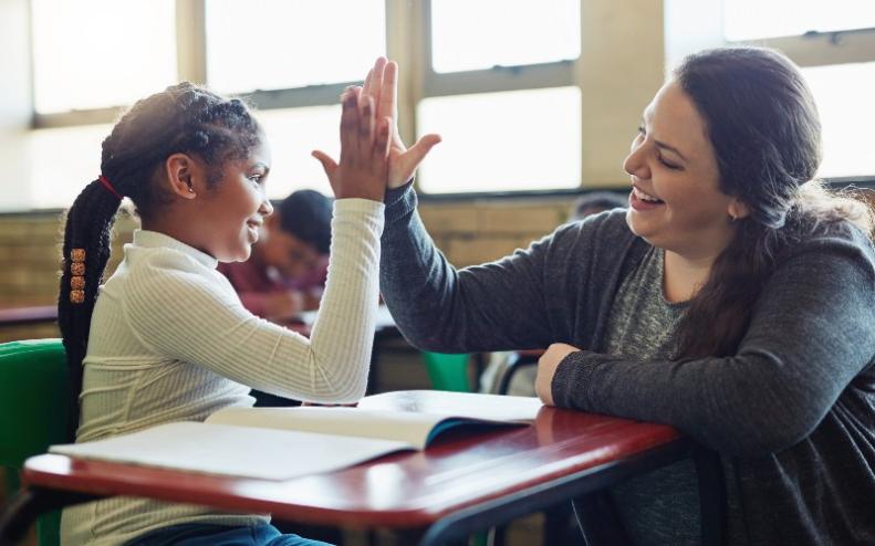 Niña dando a su maestra un high five en un aula