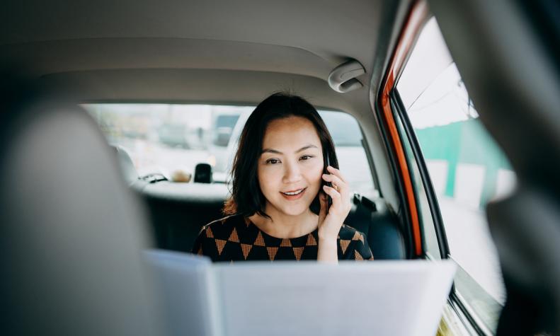 タクシーでSaaSサービスを使って仕事をするアジア人女性