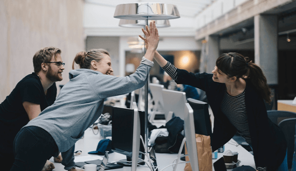 Two happy female colleagues giving high-five over desk in office