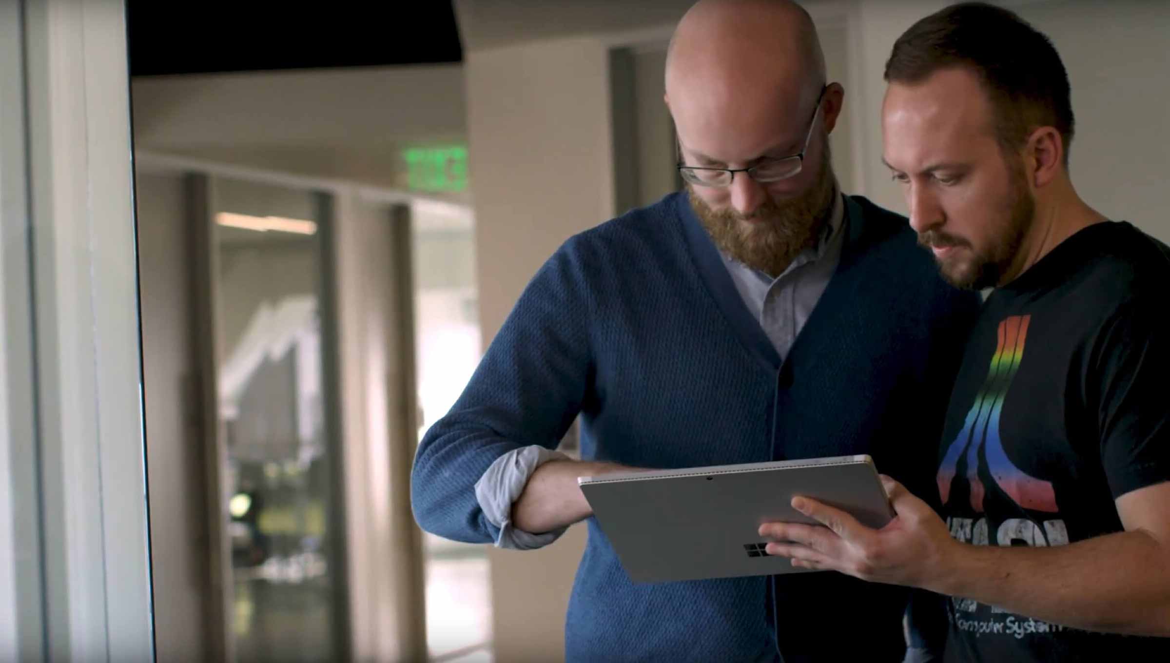 Two men looking at a Microsoft surface in an office hallway.