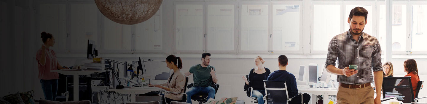 A group of people chatting at their desks in a open and bright office.