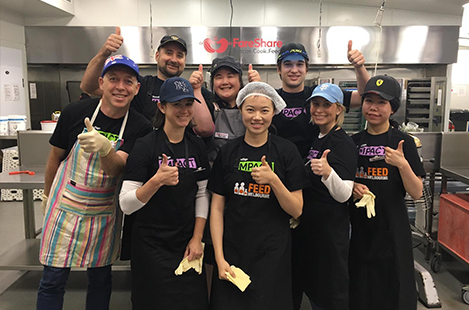 Eight DocuSign employees smiling and giving thumbs up while volunteering in a soup kitchen