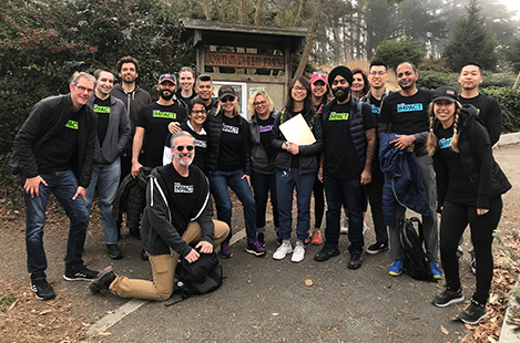 EIghteen DocuSign employees wearing DocuSign IMPACT t-shirts posing for a photo during a volunteer event at a park.
