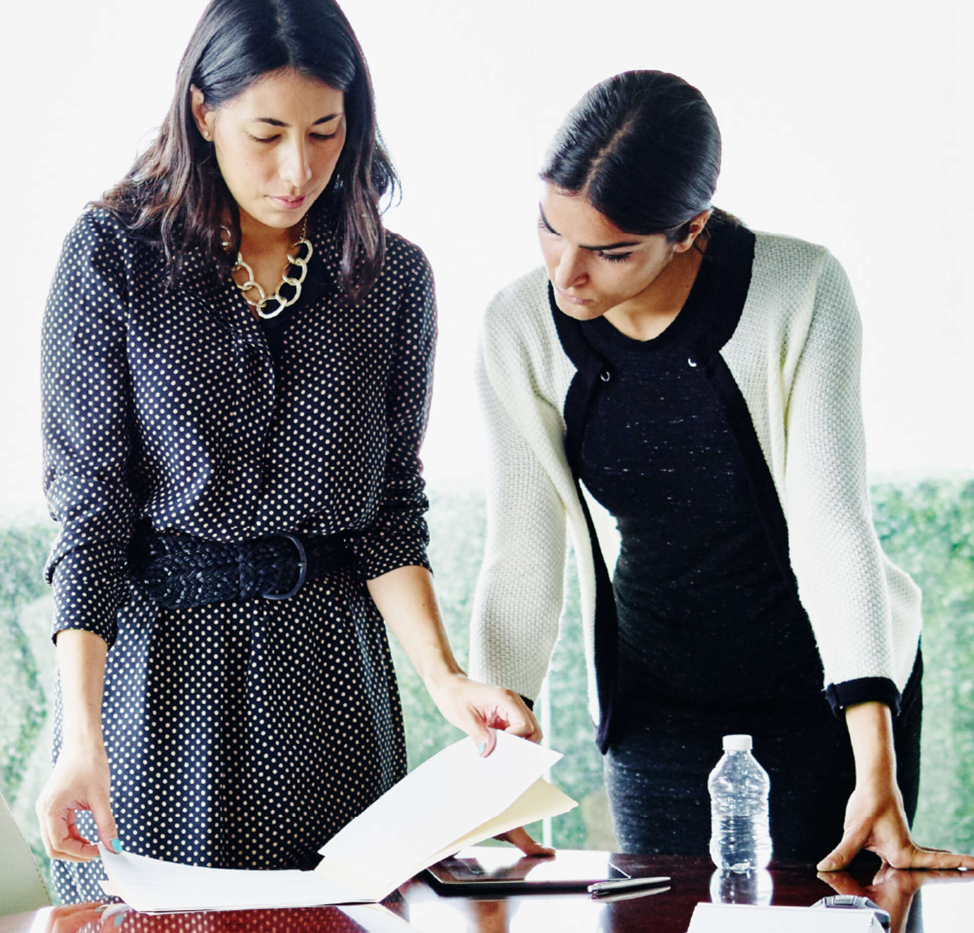 Two female coworkers standing over a conference room table looking at data.