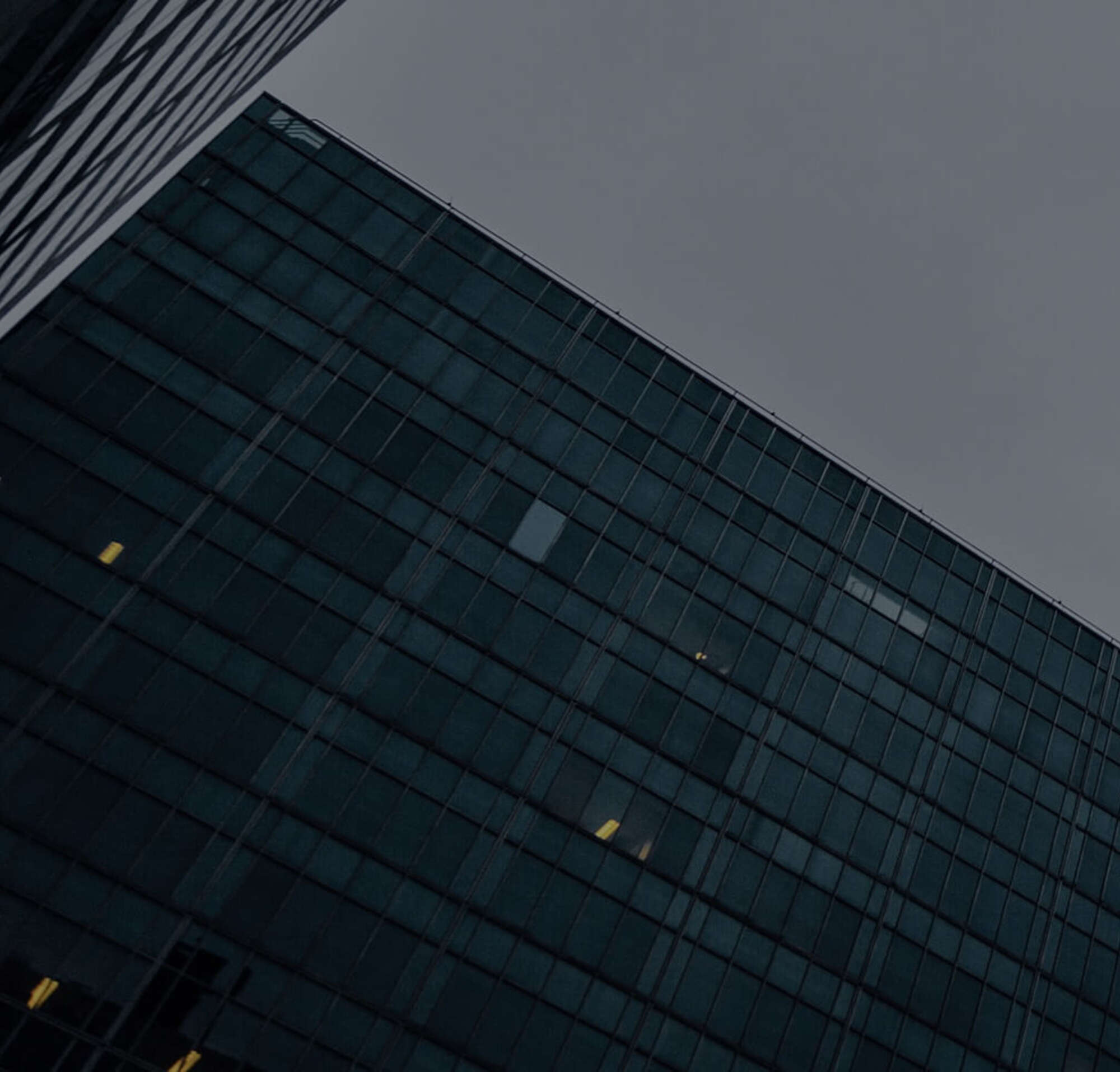 Een afbeelding in het avondlicht op een bewolkte dag aan de voet van een wolkenkrabber en een ander kantoorgebouw.