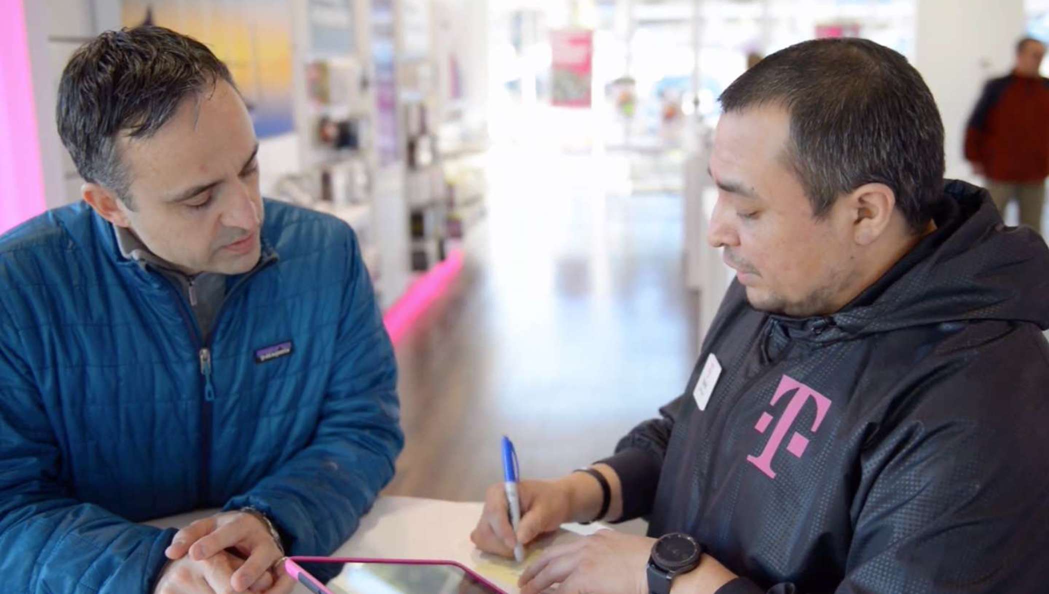 Deux personnes dans un bureau de T-Mobile relisent  un contrat téléphonique.
