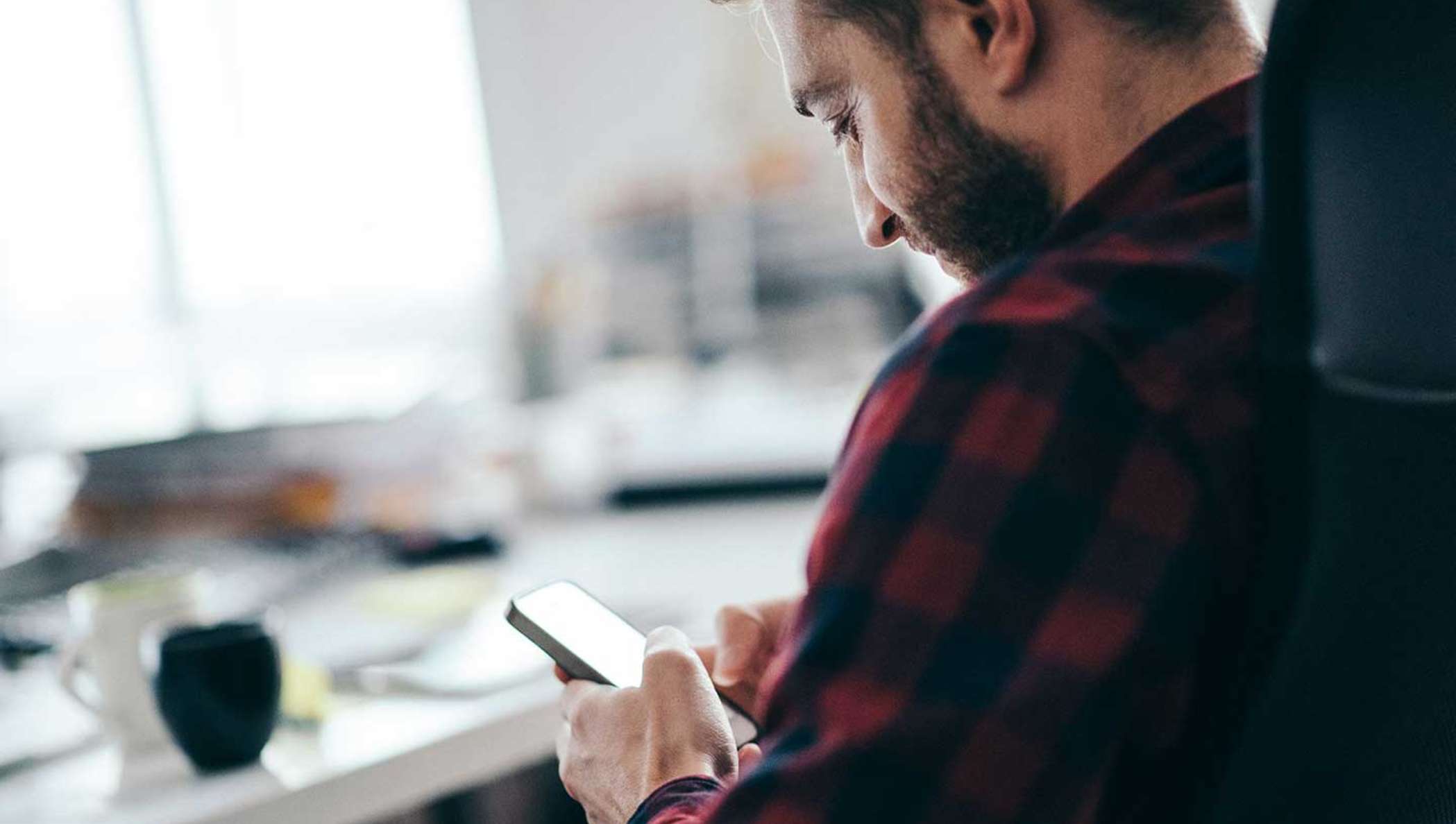 A bearded man in a flannel shirt checks the status of a document out for signature on his mobile phone